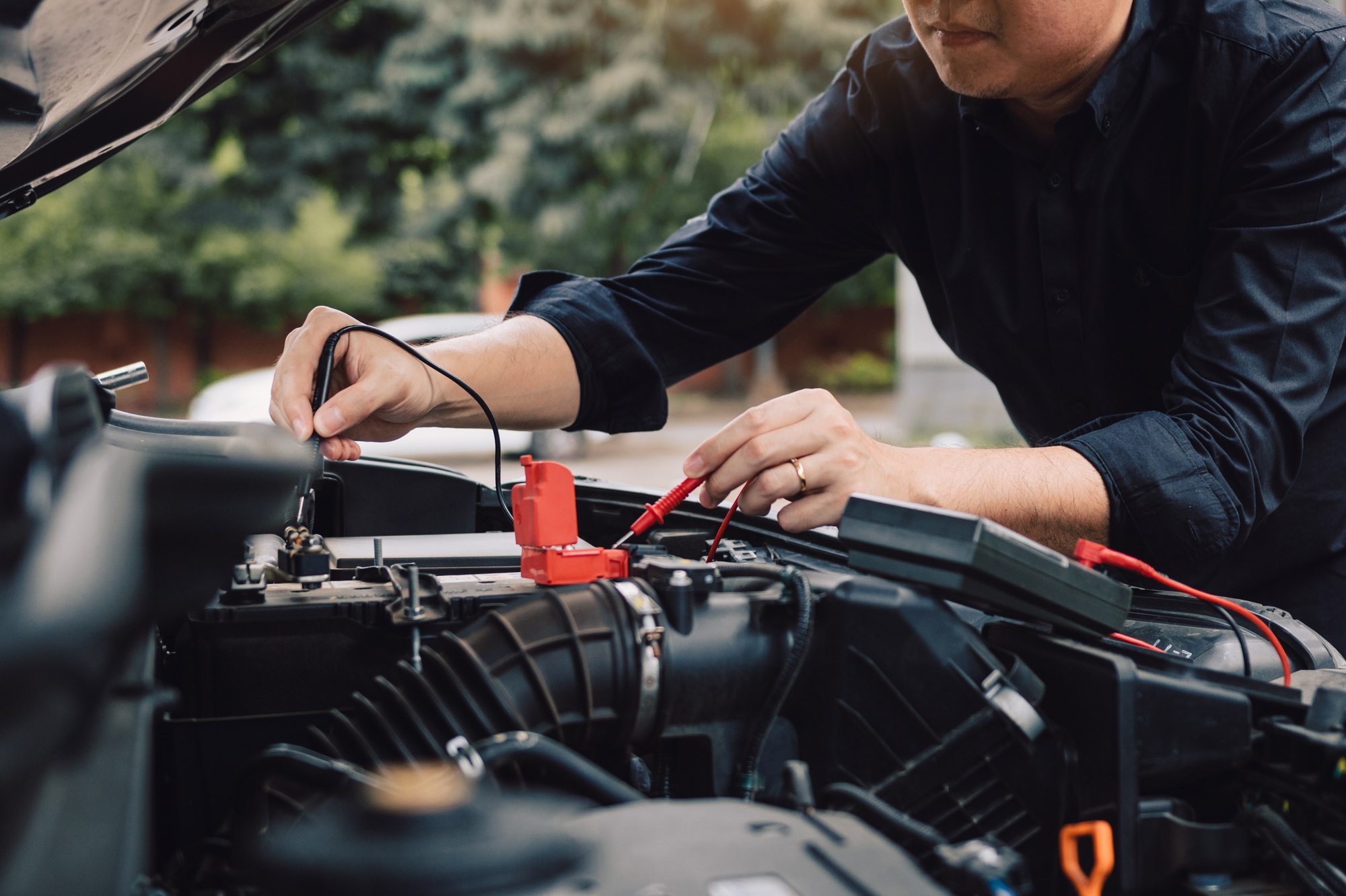 Car mechanic is using the car battery meter to measure various values and analyze it.