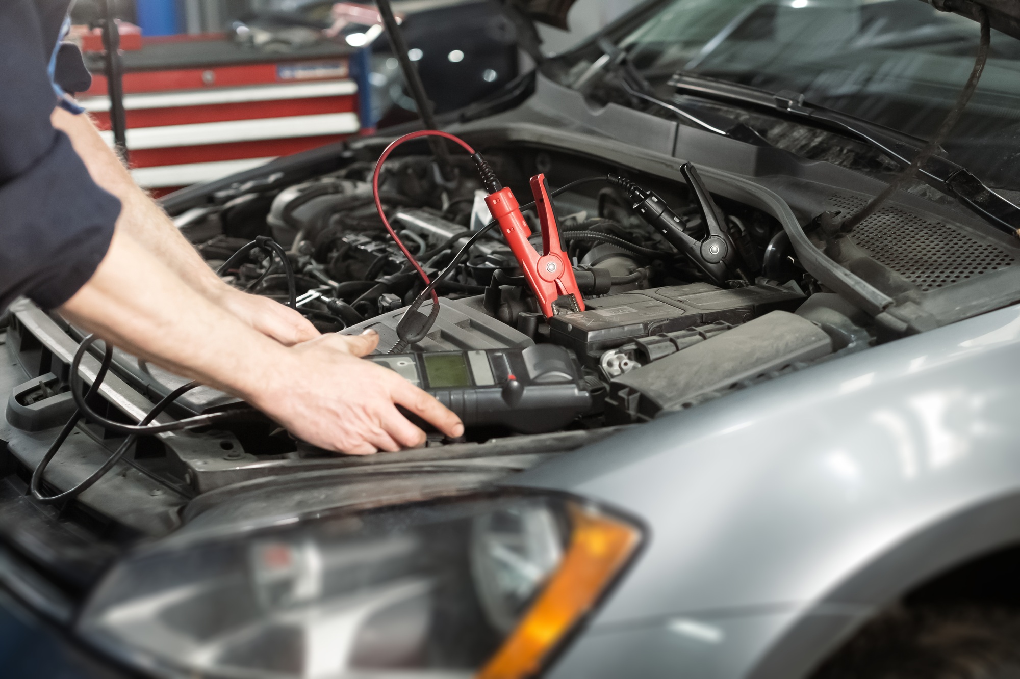 Male hands holding modern utility and checking voltage of automobile battery