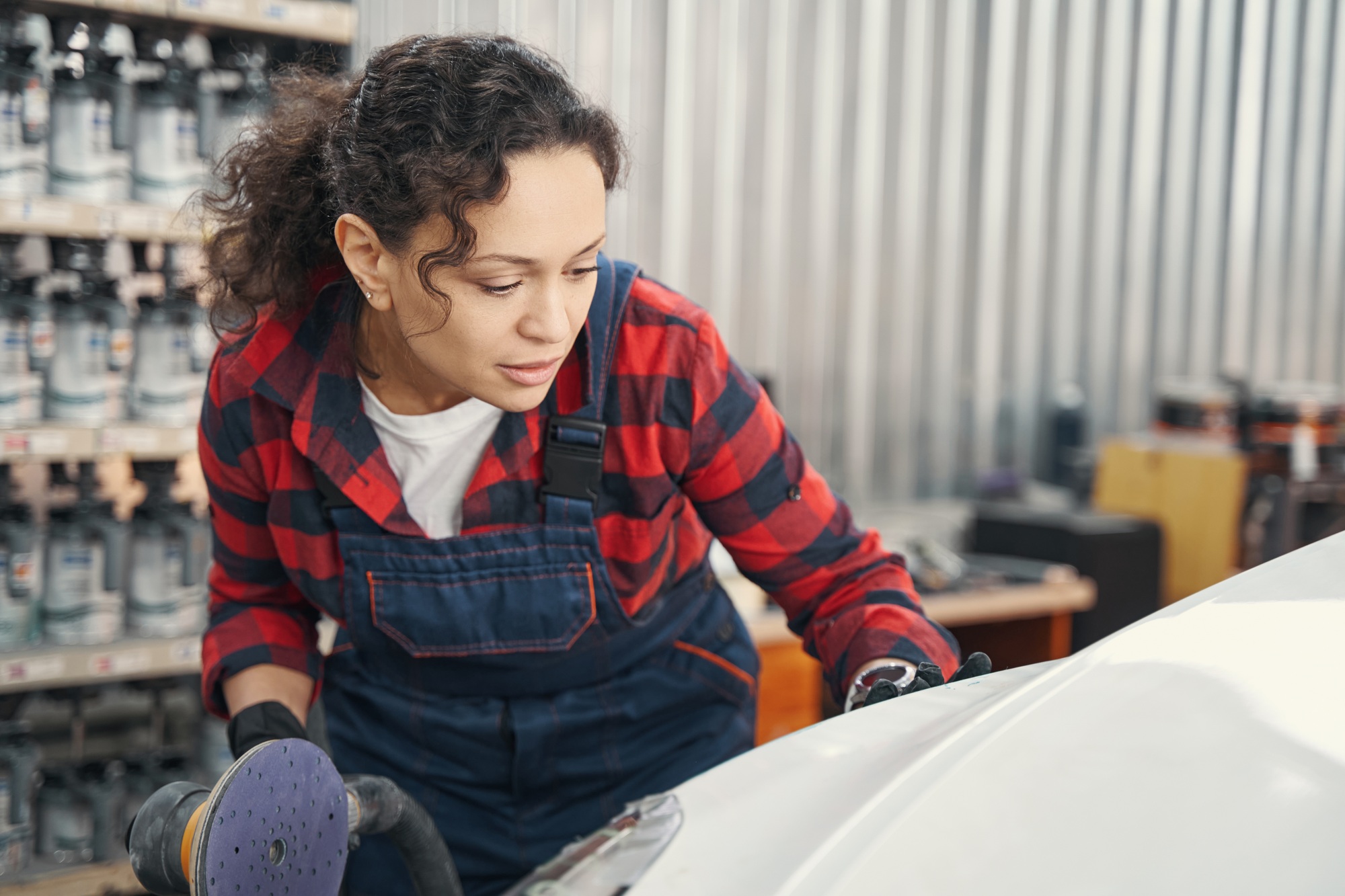 Cheerful female master cleaning car body in garage